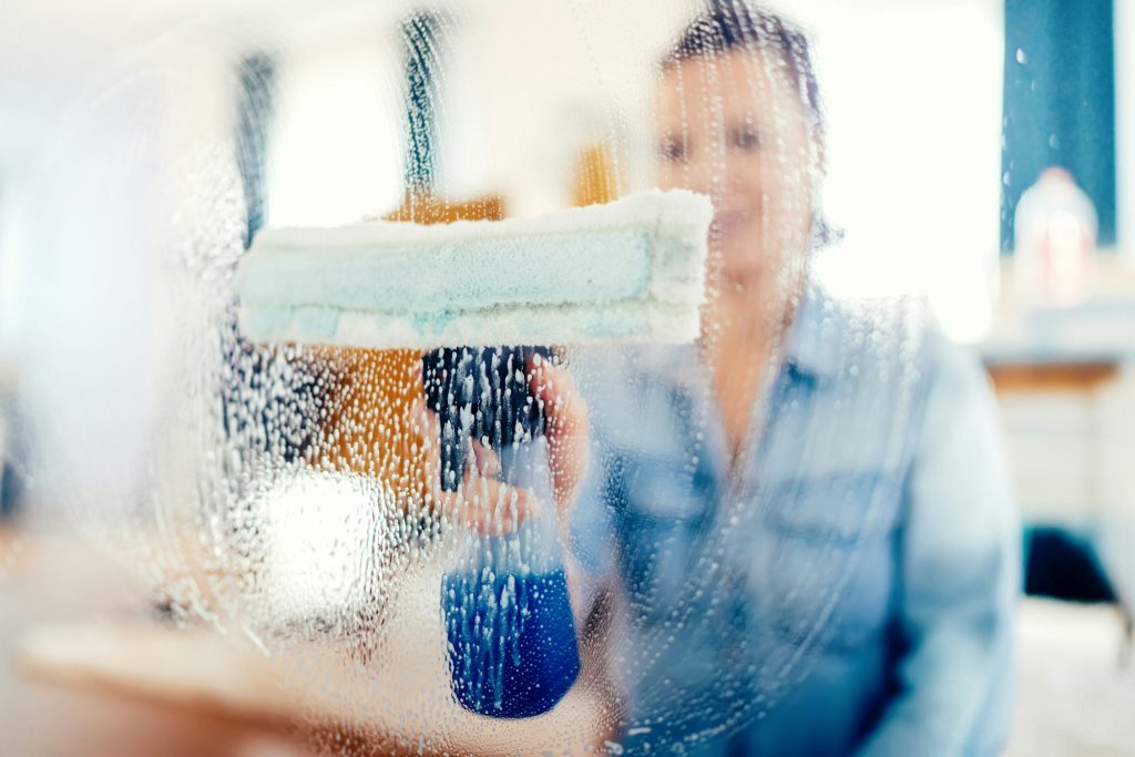 Young woman using window cleaner and doing chores around the house
